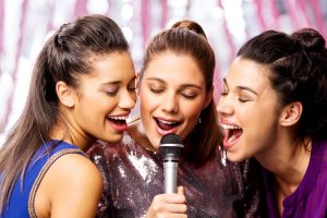 Close-up of beautiful female friends with microphone singing karaoke in nightclub. Horizontal shot.