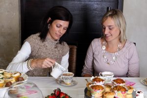 Two women friends having tea and cake. Light from the side, wall is weathered.