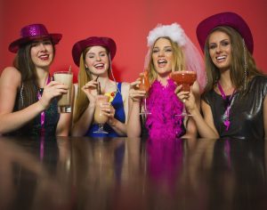 Laughing friends having hen party holding cocktails looking at camera